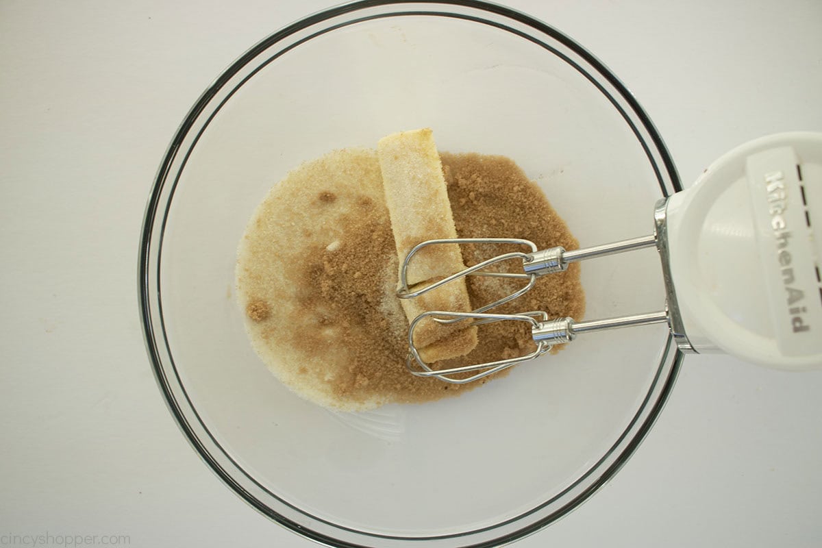 Butter and sugars in a clear mixing bowl with a hand mixer.