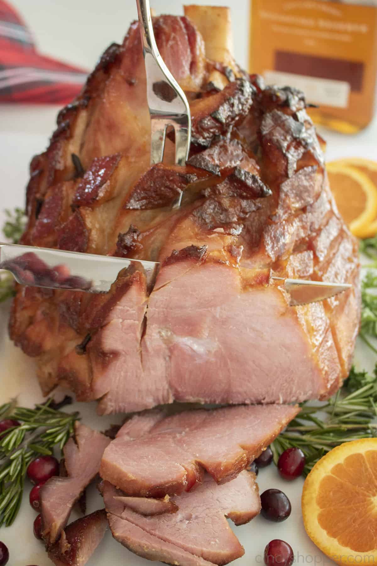Bourbon Glazed ham on a platter being held with a carving fork and being carved with a knife.