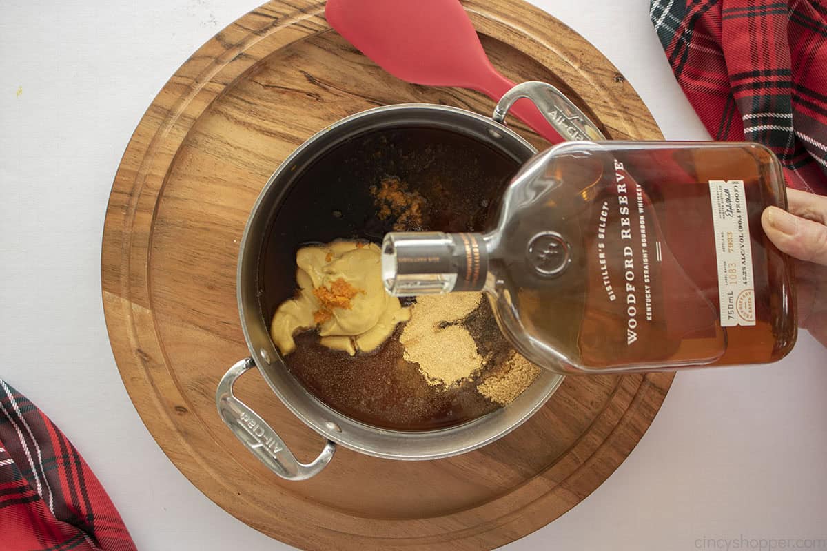 Glaze ingredients in a pan with hand pouring bourbon on top.