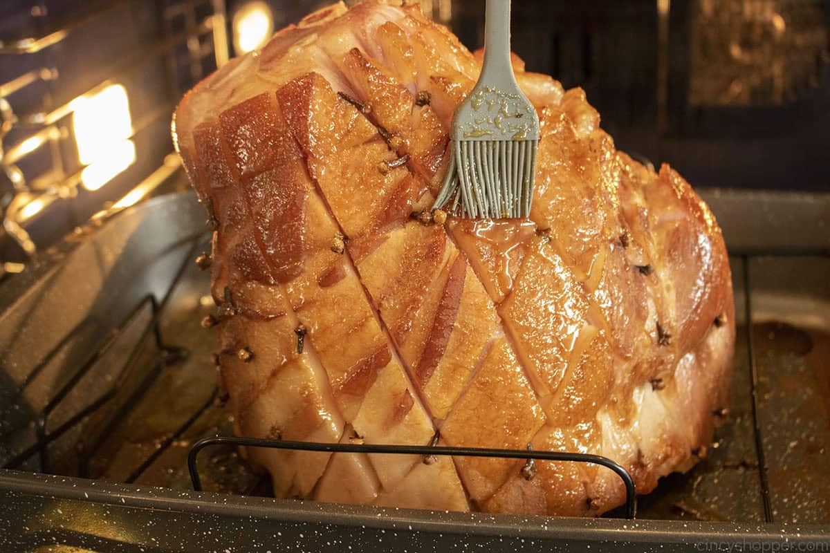 Ham in the oven being brushed with bourbon glaze.