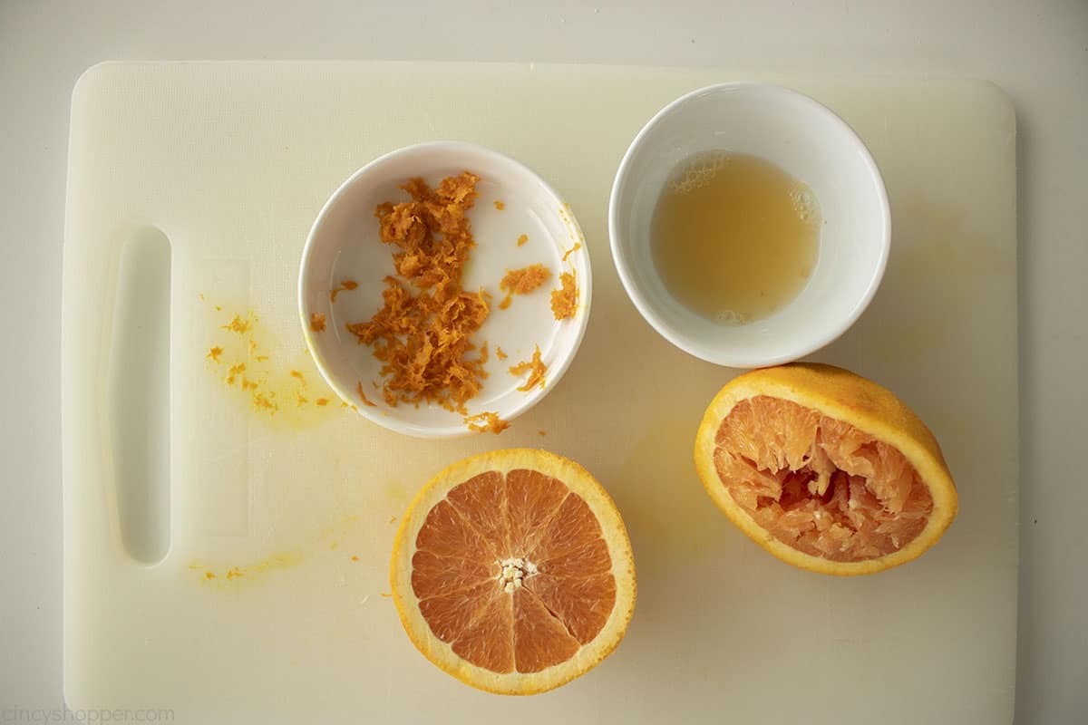 Oranges with zest and juice on a cutting board.