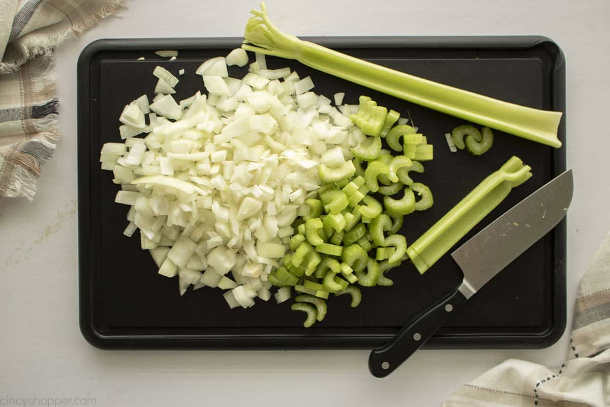 Chopped onions and celery on a black cutting board with knife.