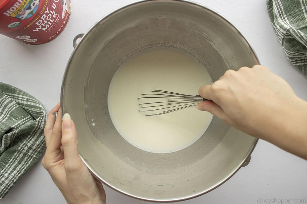 Whisking water and powdered milk in a mixing bowl.