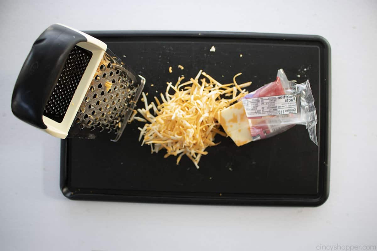 Cheese grater on a cutting board with shredded colby cheese.