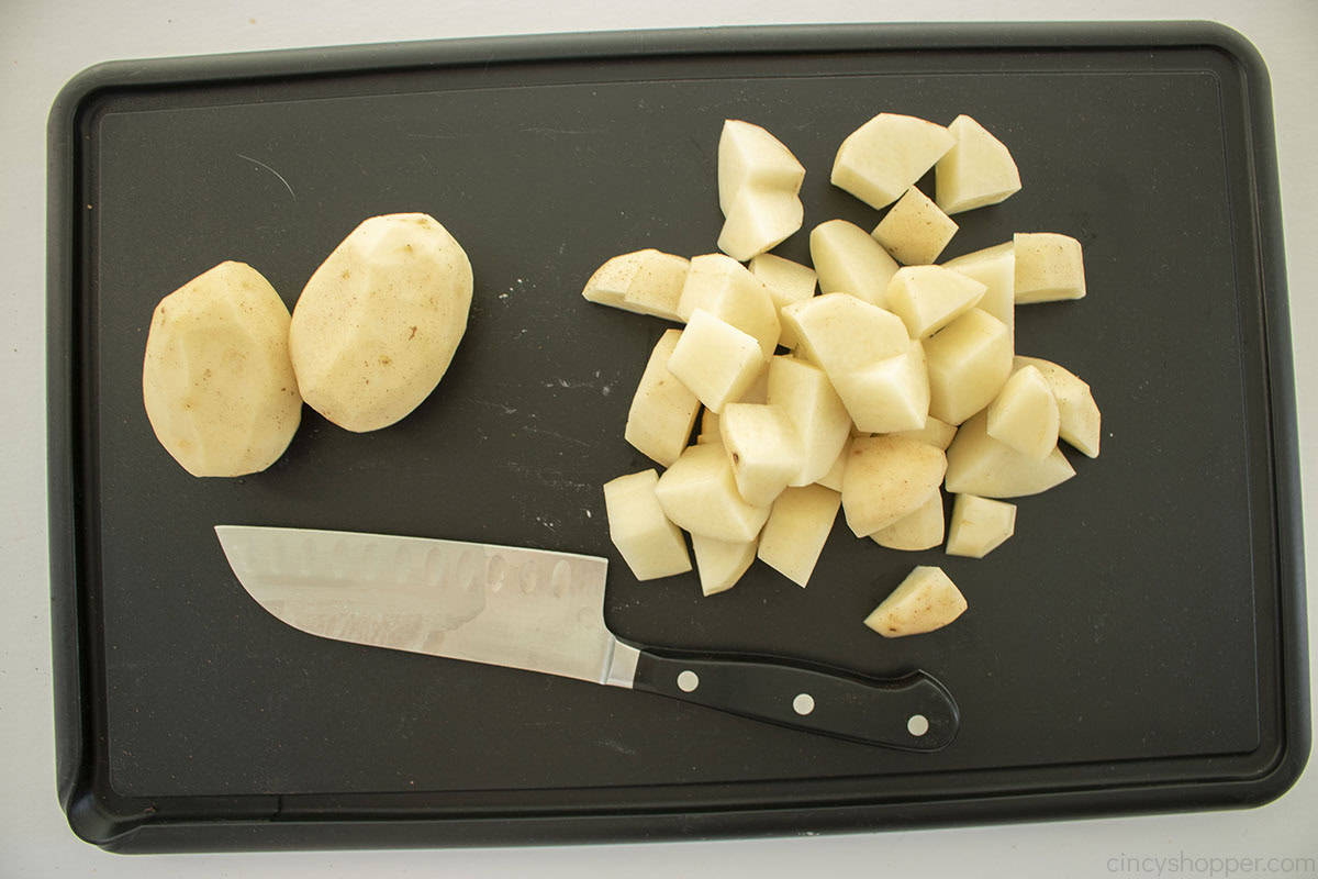 Peeled potatoes on a cutting board being diced.