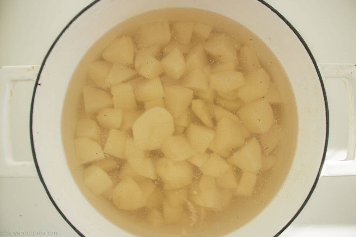Cubed potatoes boiled in a white pot.