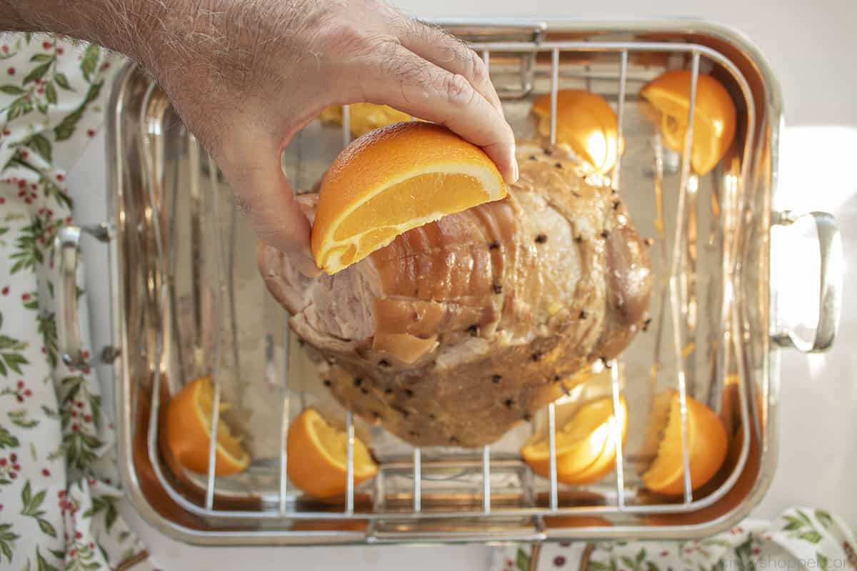Squeezing orange juice on to the top of uncooked ham.