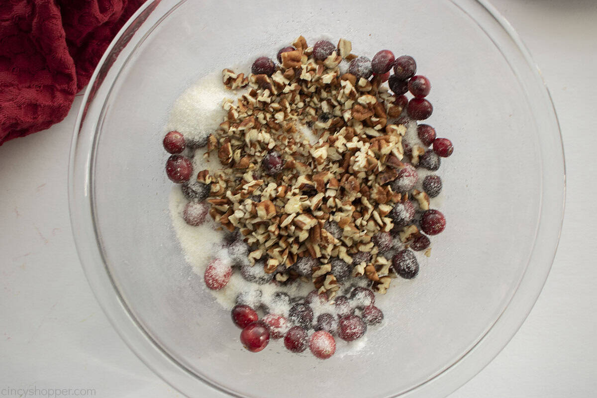 Fresh cranberries, pecans and sugar in clear mixing bowl.