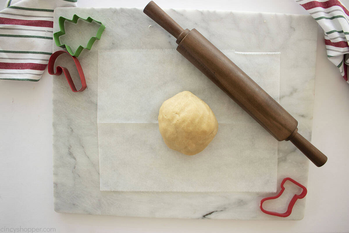 Sugar Cookie dough ball on a piece of parchment paper with a rolling pin.