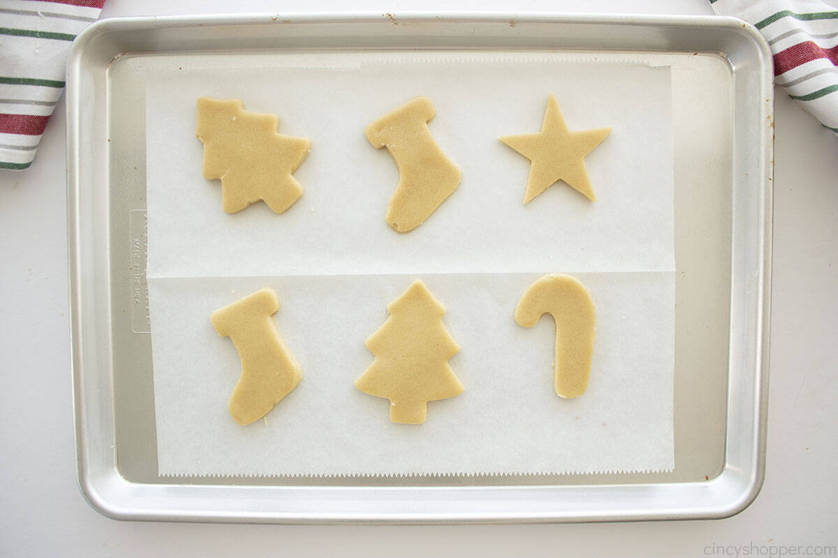 Cut-out shapes of cookies on parchment paper that is on a cookie sheet.