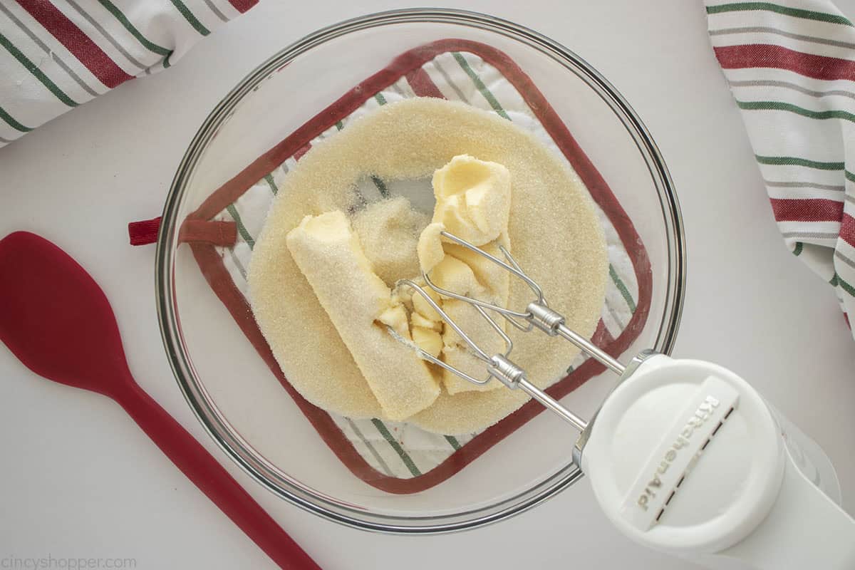 Butter and sugar being creamed in a clear mixing bowl with a hand mixer.