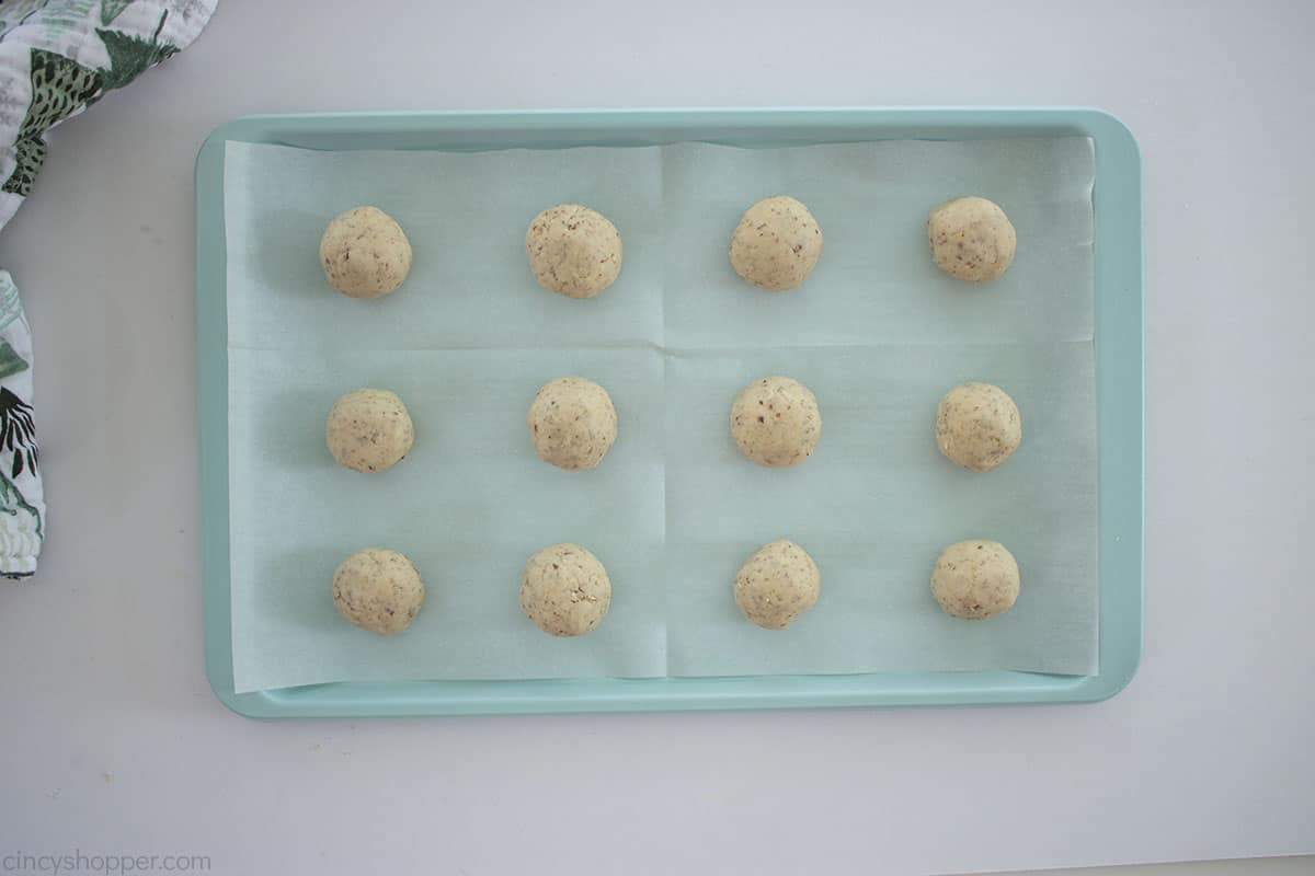 Snowball cookie dough on parchment lined baking sheet.