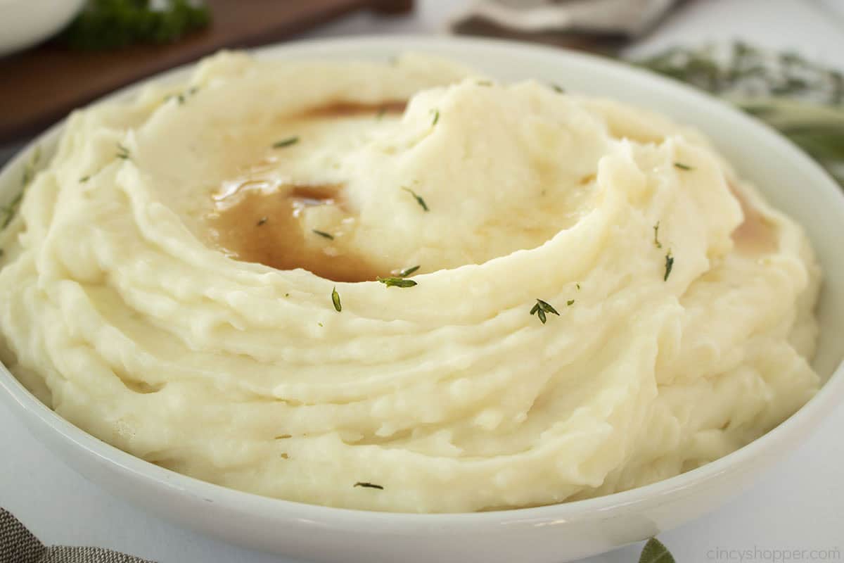 Mashed potatoes in a bowl with fresh herbs and browned butter on top.