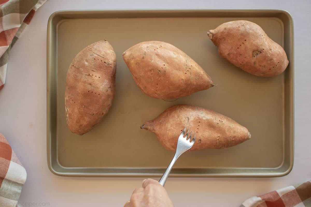Sweet potatoes on a pan with a fork piercing them.