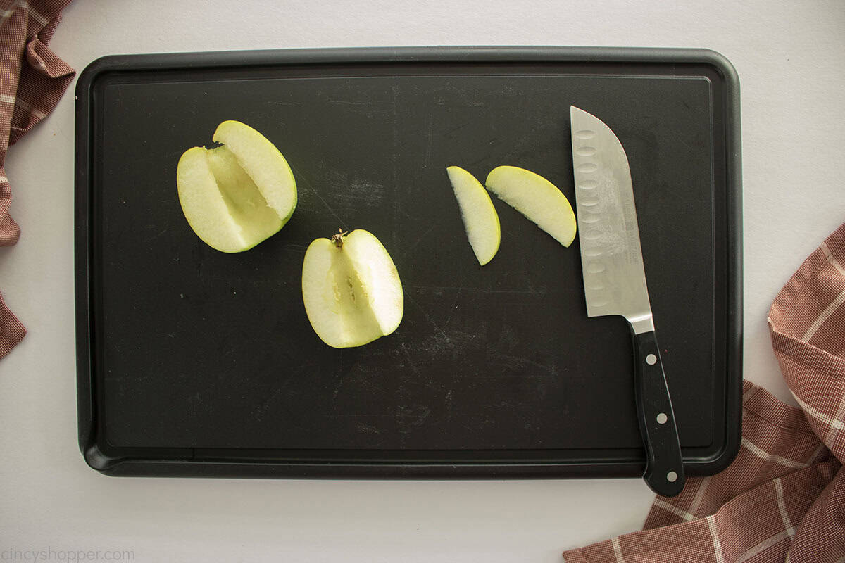 Cored and sliced apples on a cutting board with knife.