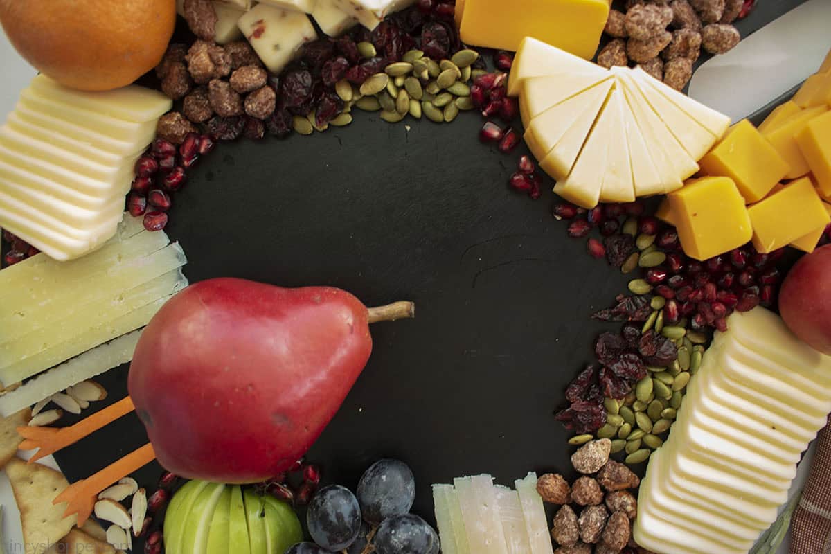 Turkey body placed on black charcuterie board with nuts, fruit and cheeses.