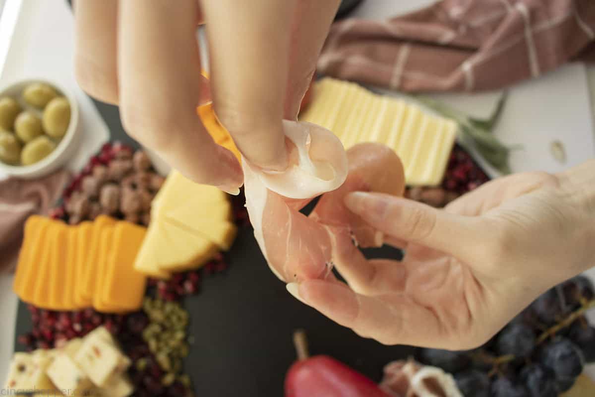 Hands showing how to wrap prosciutto meat.