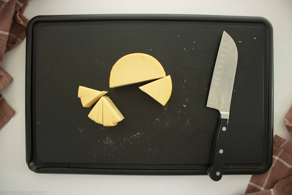 Round Gouda cheese on a cutting board being cut with knife.