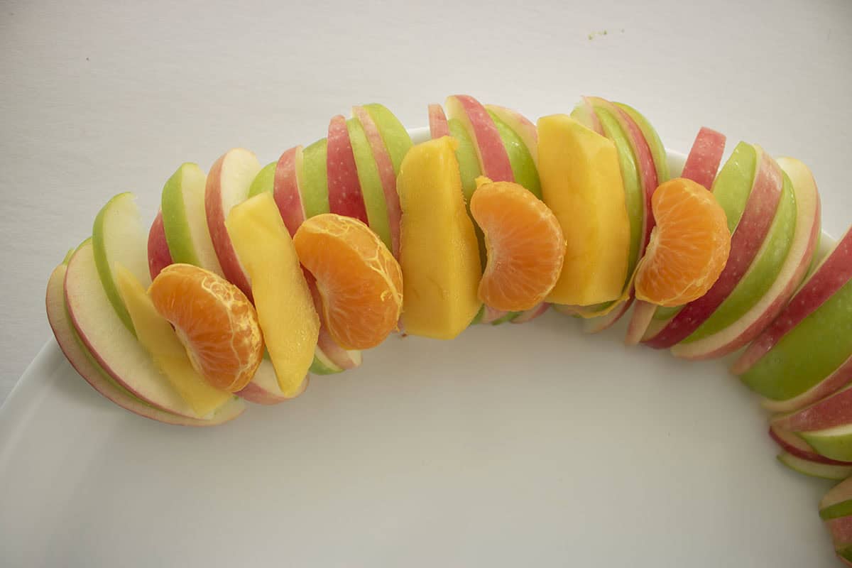 Mango and orange slices placed on top of apples.