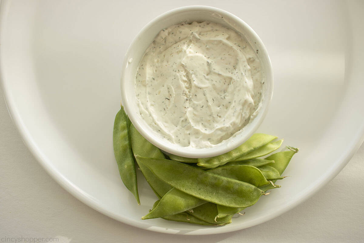 Dip in a white bowl on a white tray and snow peas.