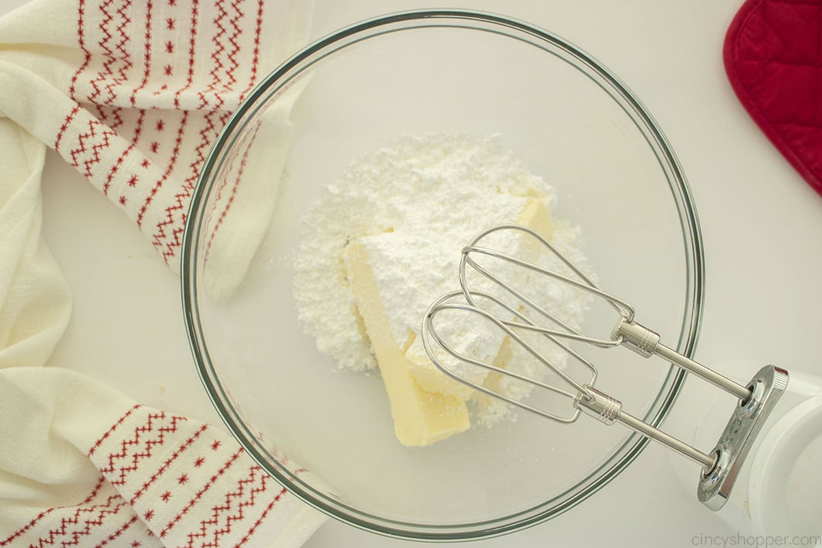 Butter and powdered sugar in mixing bowl with hand held mixer.