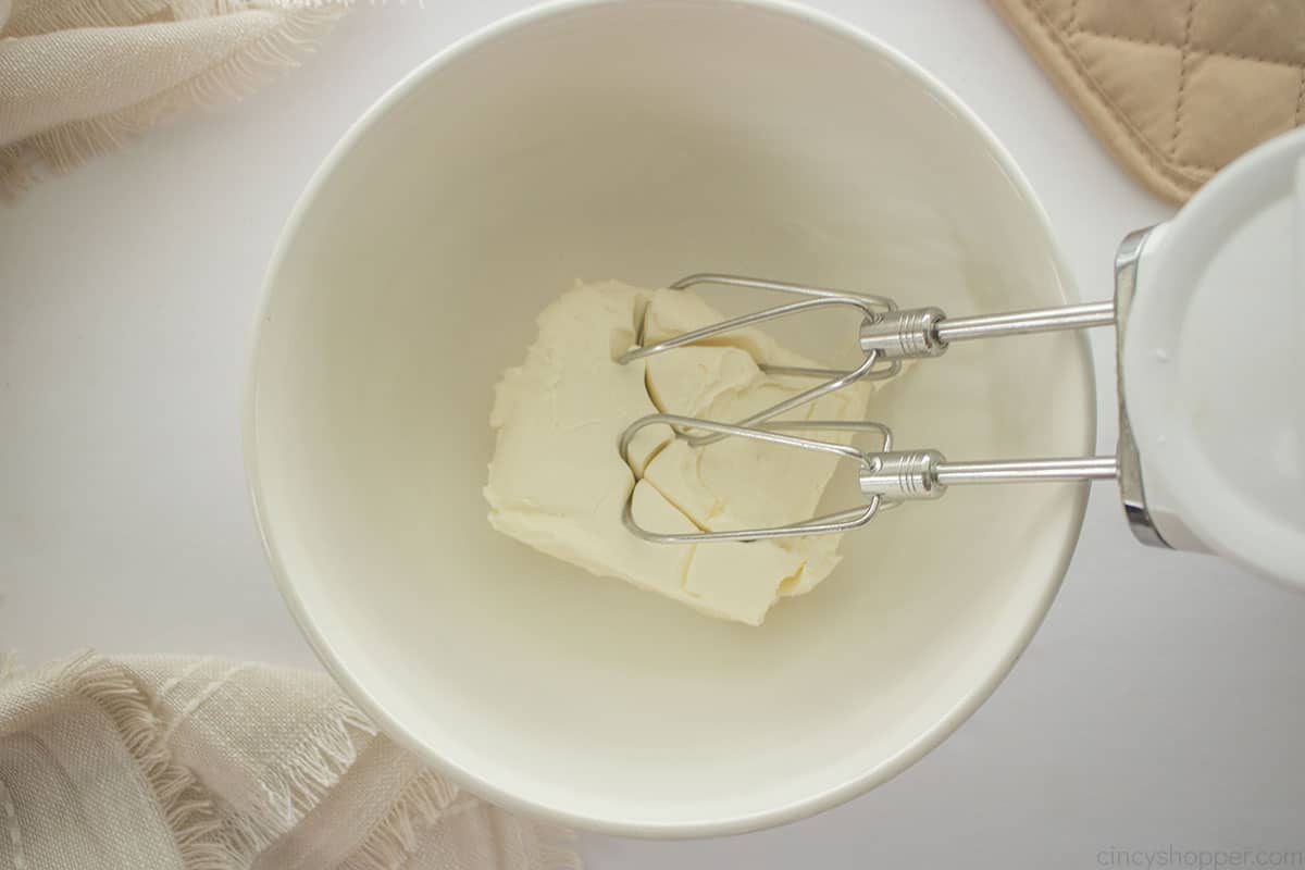 Cream chees ein a mixing bowl with a hand mixer.