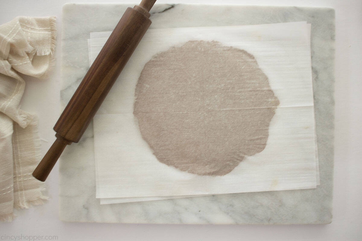 Rolled out gingerbread cookie dough between two sheets of parchment paper.