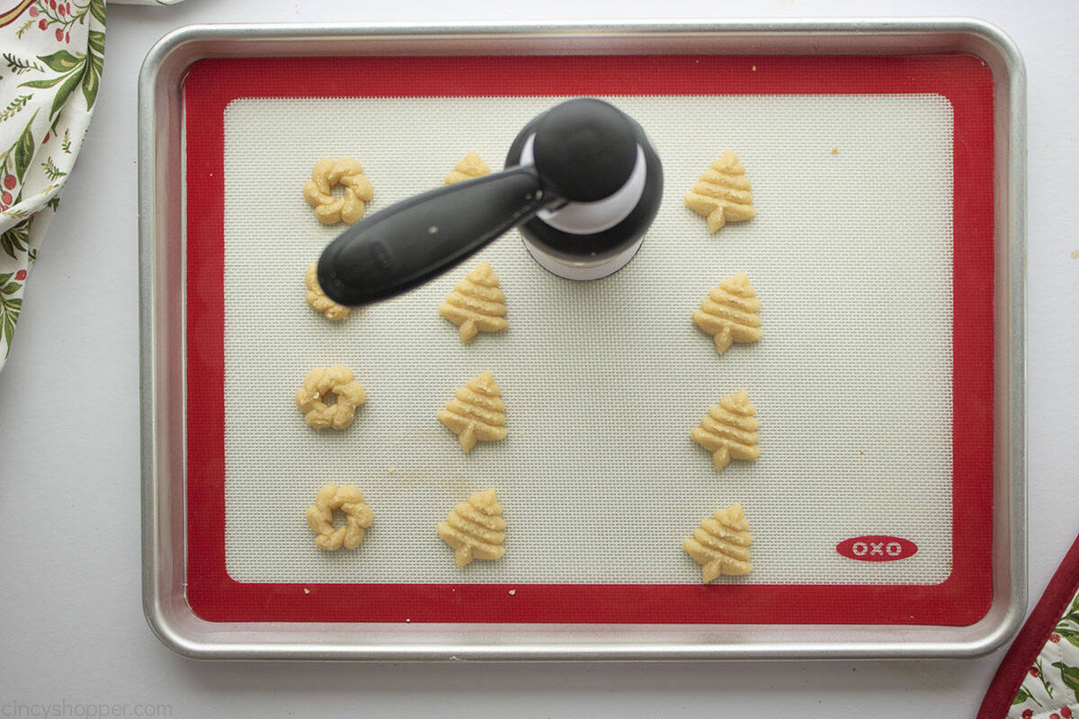 Cookie press with Spritz Cookie dough on a silicone mat lined cookie sheet.