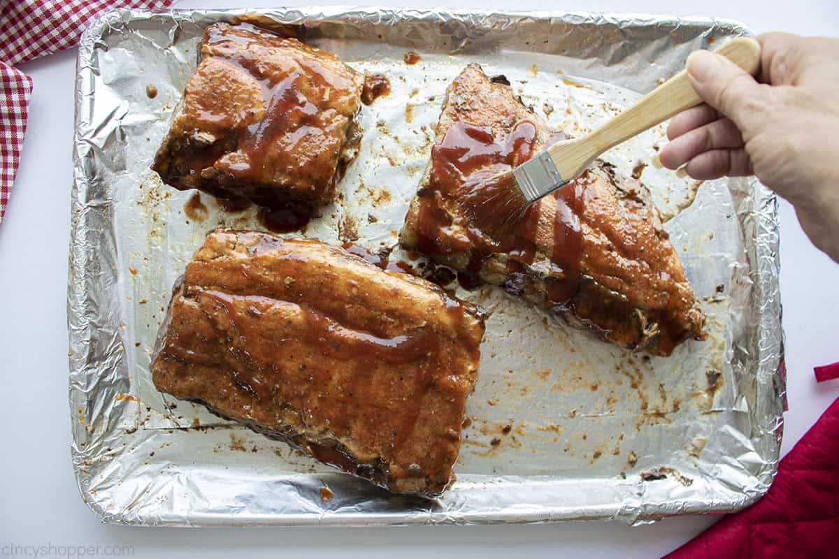 Basting baby back oven ribs with BBQ sauce.