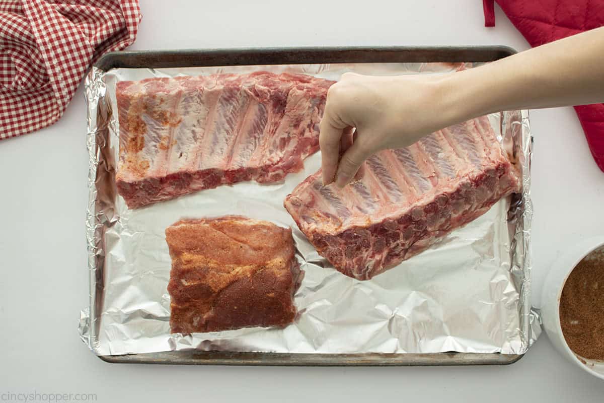 Adding pork rub to back ribs.